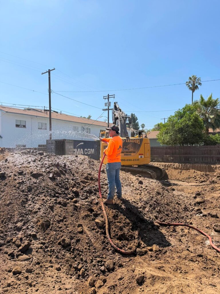 Worker watering excavation area to control dust before re-compaction _ Demoleaders